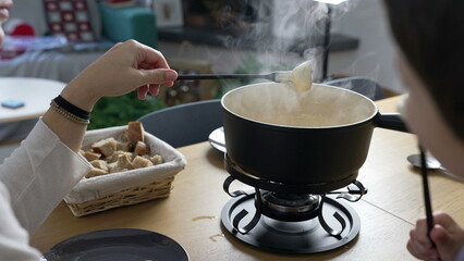 Traditional Swiss Fondue - people eating pieces of bread with cheese at home, close-up of European dish from Switzerland