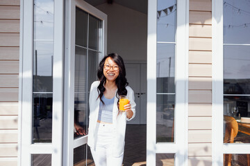 Asian woman opens glass door and goes out onto veranda of house