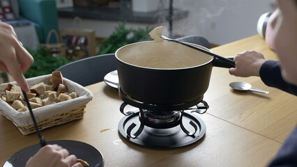 Traditional Swiss Fondue - people eating pieces of bread with cheese at home, close-up of European dish from Switzerland
