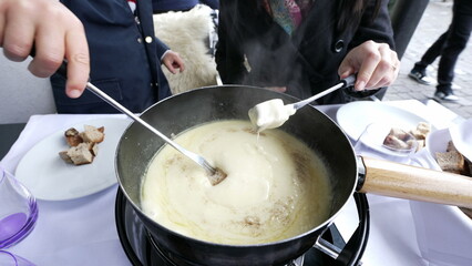 Swiss fondue - closeup of hands eating bread with cheese at restaurant meal, traditional European food during winter season, child and mother