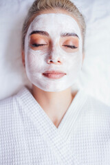 Beautiful young woman lying with her eyes closed and white rejuvenating mask