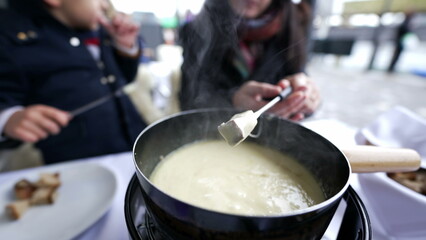 Obraz na płótnie Canvas Traditional Swiss food, closeup hand holding fork with bread dipping in cheese, peopel enjoying winter food in cold weather