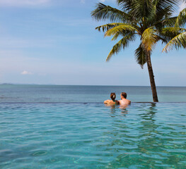 Young couple relaxing in infinity pool under coco palms