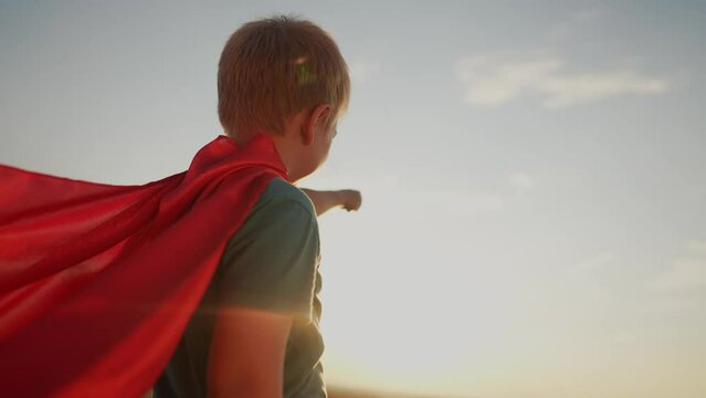 boy with the cloak. concept of a happy childhood and family for a child. a child in a superhero costume stretched his hand forward, a red cape and a blue T-shirt, lifestyle sunset on the background