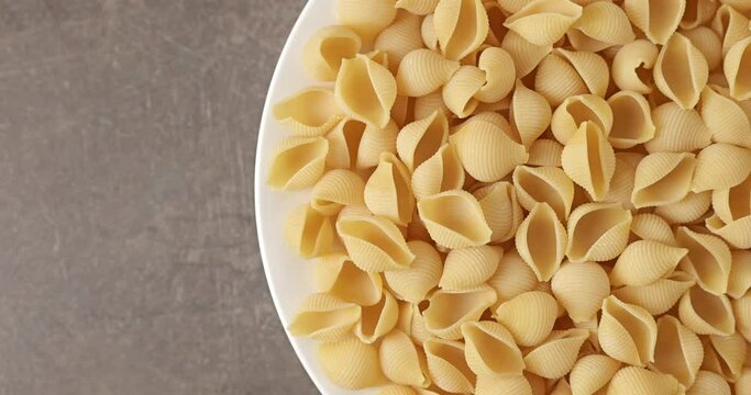 Dry conchiglie rigate pasta on a white plate, copy space