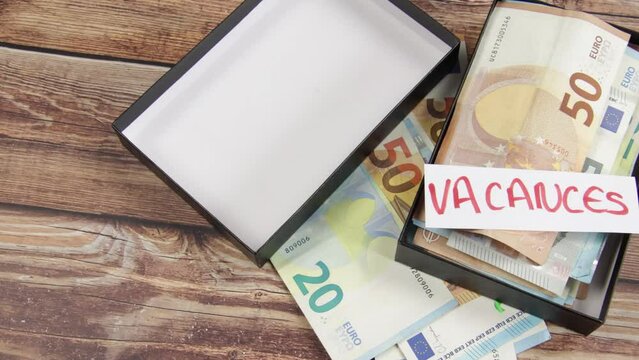 boite rempli de billets de banque avec un papier avec &eacute;crit dessus "vacances" en fran&ccedil;ais
