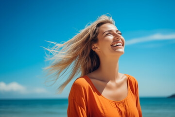 Fototapeta na wymiar Beautiful young caucasian woman with long blonde hair looking up at the sky smiling, dressed in orange shirt, turquoise water beach background