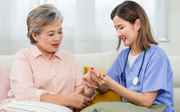 Two Asian nurse and female senior old aged woman smiling with happiness, sitting on sofa at home, doing physical therapy, consulting. Nursing or caring home, Aging, Retirement Concept.