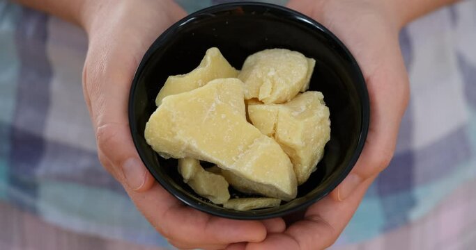 A woman holding a black bowl with organic cocoa butter in it in her hands. Close up.