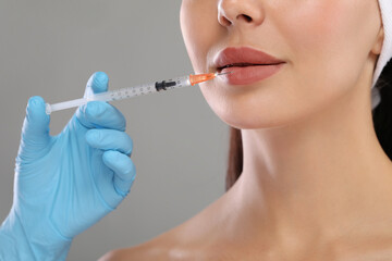 Doctor giving lips injection to young woman on light grey background, closeup. Cosmetic surgery