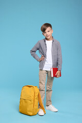 Cute schoolboy with book on light blue background