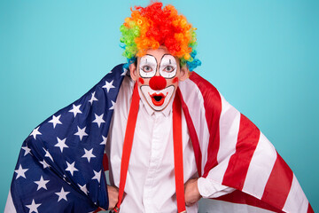 A funny clown with colored hair wrapped himself in the flag of America. Blue background....
