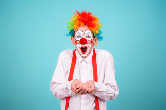 A joyful clown. A cute man in a suit and makeup for a holiday for children. A fool. Blue background. Copy the space.