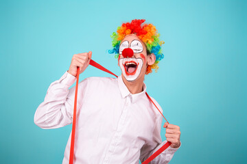 A joyful clown. A cute man in a suit and makeup for a holiday for children. A fool. Blue background. Copy the space. - obrazy, fototapety, plakaty