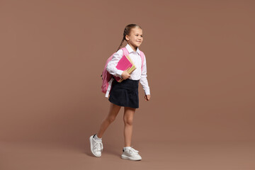 Fototapeta na wymiar Happy schoolgirl with backpack and books on brown background