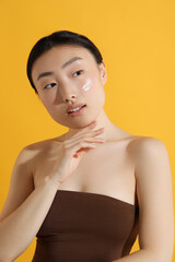 Beautiful young woman with sun protection cream on her face against orange background