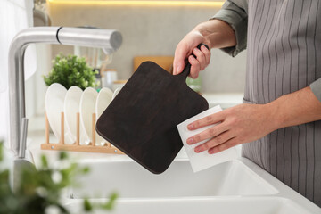 Man wiping dark wooden cutting board with paper napkin at sink in kitchen, closeup