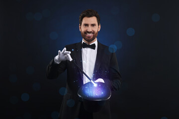 Smiling magician showing trick with top hat and wand on dark blue background