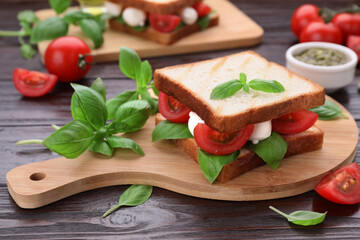 Delicious Caprese sandwich with mozzarella, tomatoes, basil and pesto sauce on wooden table