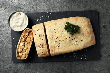 Delicious strudel with chicken and vegetables served on grey textured table, top view