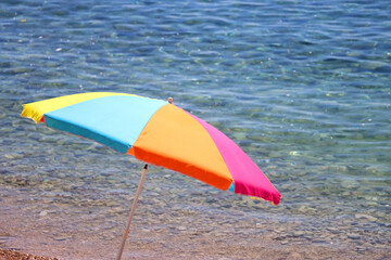 Colorful parasol on the beaach, by the sea. Sunny summer day. Selective focus.