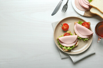 Plate of tasty sandwiches with boiled sausage, tomato and lettuce on white wooden table, flat lay....