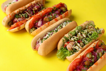 Delicious hot dogs with different toppings on yellow background, closeup