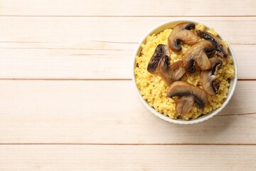 Tasty millet porridge and mushrooms in bowl on light wooden table, top view. Space for text