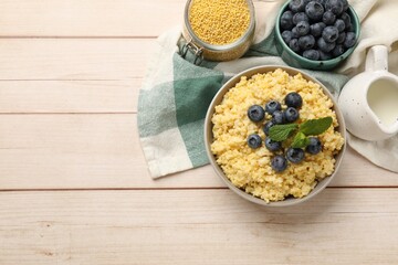 Tasty millet porridge with blueberries and mint in bowl on light wooden table, flat lay. Space for text