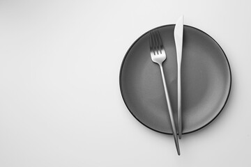 Plate, fork and knife on white background, top view. Space for text