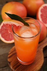 Tasty grapefruit drink with ice in glass and fresh fruits on wooden table, closeup