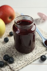 Tasty baby food in jar, blueberries and apples on white table