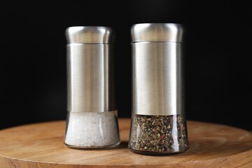 Salt and pepper shakers on wooden board against black background, closeup