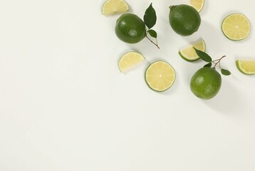 Limes and green leaves on white background, flat lay. Space for text