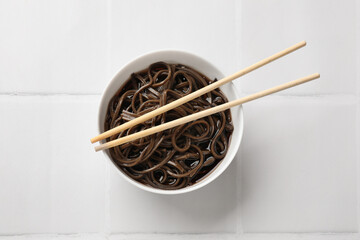 Tasty buckwheat noodles (soba) with sauce in bowl and chopsticks on white tiled table, top view