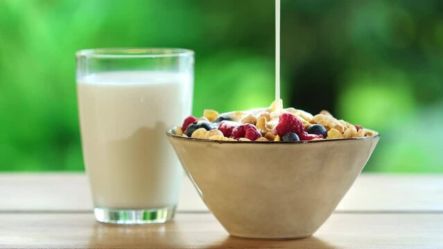 Milk or yogurt pouring into bowl with corn flakes. Morning breakfast is served with bowl oatmeal, muesli, granola, honey, glass of milk drink. Concept of Diet, Organic Nutrition, Healthy Food