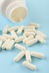 Bottle and vitamin capsules on light blue background, closeup
