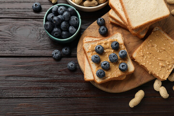 Delicious toasts with peanut butter, blueberries and nuts on wooden table, flat lay. Space for text