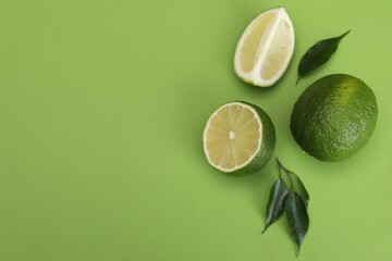 Flat lay composition with fresh limes and leaves on green background. Space for text