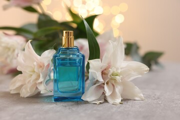 Fototapeta na wymiar Bottle of perfume and beautiful lily flowers on table against beige background with blurred lights, closeup