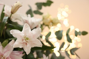 Bouquet of beautiful lily flowers against beige background with blurred lights, closeup. Space for text