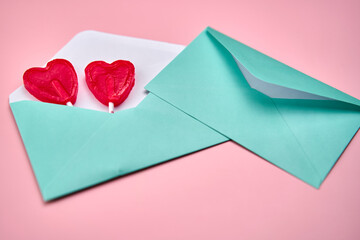 Love letter with two heart-shaped red lollipops inside on a pink background