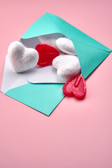 Blue envelope with a bunch of hearts and lollipops inside on a pink surface. Valentine's Day composition.