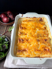 Spinach and Ricotta Lasagne Rolls (front view) with salad and red onions by the side on a wooden surface
