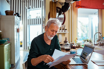 Senior man reading bill document at home kitchen