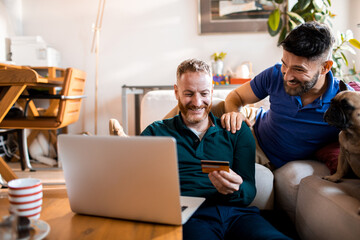 Gay couple shopping online at home with credit card and laptop
