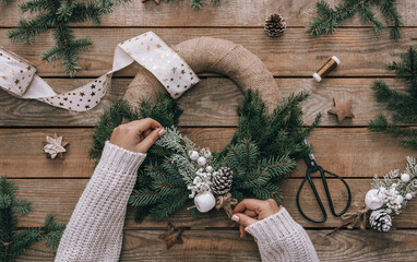 Top view of female hands making Christmas wreath on wooden background