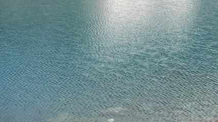 Ripples on the water of a blue mountain lake. Rocks at the bottom shine through the clear water. A beautiful mountain lake. Wild picturesque nature.