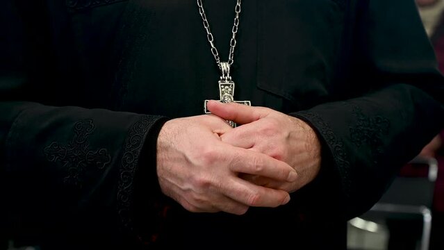 Catholic priest in liturgical vestments praying with hands folded in cathedral. Christian priest with a cross on his neck.