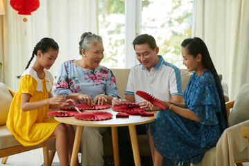 Three generation family making red paper fans to decorate house for Tet